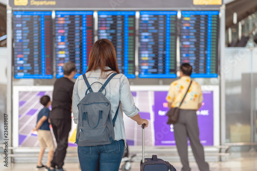 Obraz na płótnie Back side of asian woman traveler with luggage standing over the flight board for check-in at the flight information screen in modern an airport, travel and transportation concept w salonie