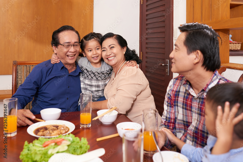 Happy grandparents hugging their granddaughter at dinner table Happy grandparents hugging their granddaughter at dinner table