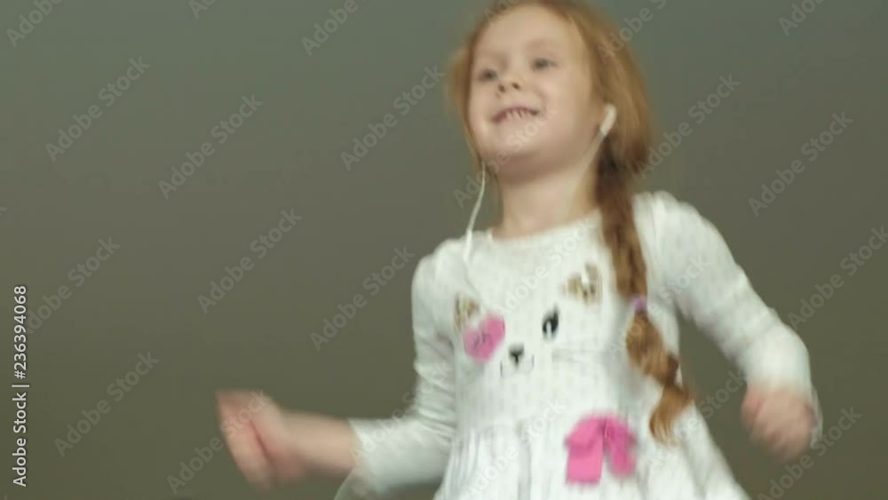 little crazy girl in headphones jumping, dancing on the sofa in the room little crazy girl in headphones jumping, dancing on the sofa in the room