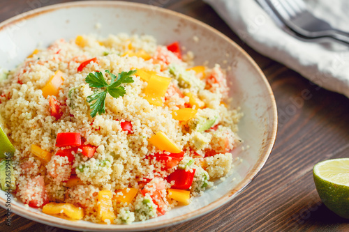 Couscous salad with fresh red and yellow bell peppers, avocado, tomatoes and lime. The concept of vegetarian and healthy food.