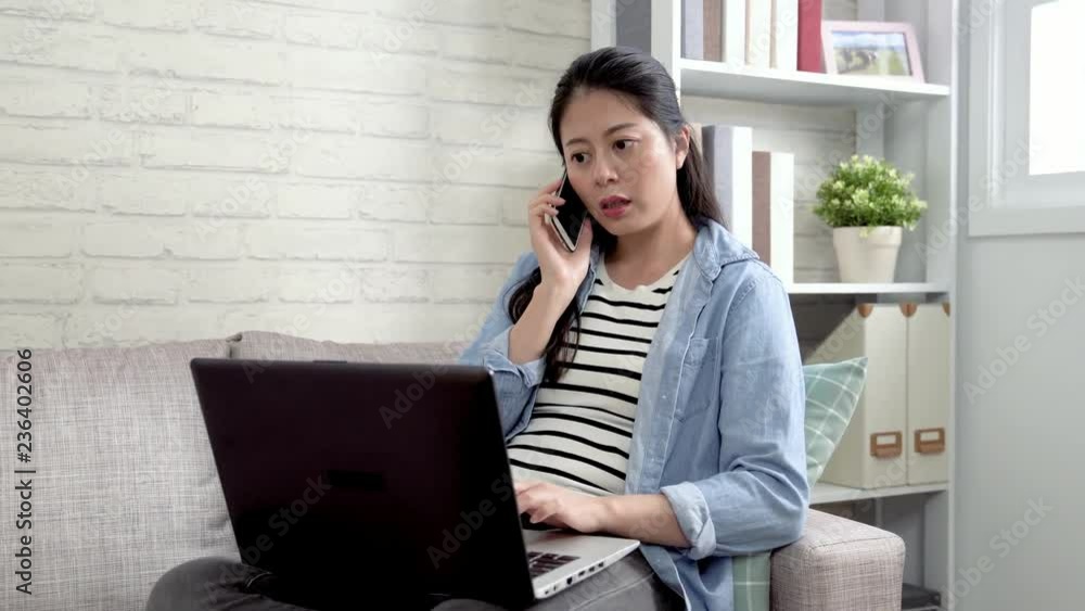 confident asian woman talking on smartphone while working at home office sitting in sofa using laptop computer. elegant lady dealing with problem on bank online service teaching the way to check bill confident asian woman talking on smartphone while working at home office sitting in sofa using laptop computer. elegant lady dealing with problem on bank online service teaching the way to check bill