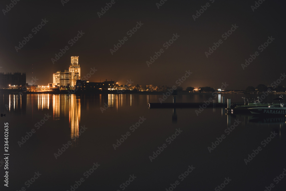 September 3, 2017 - Al Hamra Village in Ras al Khaimah, United Arab Emirates. Night view of water front in Persian gulf with pier, boats and Illuminated arabian luxury hotel reflected in the sea.