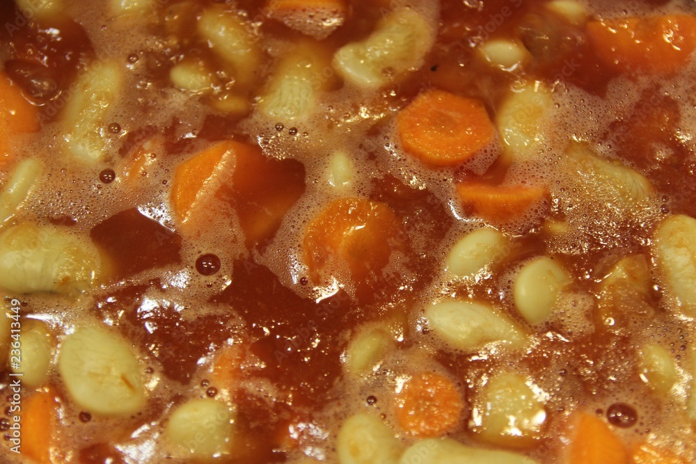Close up boiling traditional greek bean soup in a pot with carrots and red tomato sauce Close up boiling traditional greek bean soup in a pot with carrots and red tomato sauce