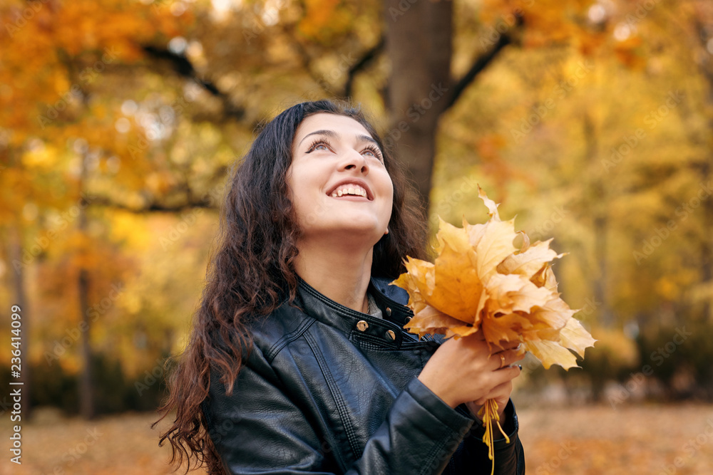 Pretty woman is posing with bunch of maple's leaves in autumn park. Beautiful landscape at fall season. Pretty woman is posing with bunch of maple's leaves in autumn park. Beautiful landscape at fall season.