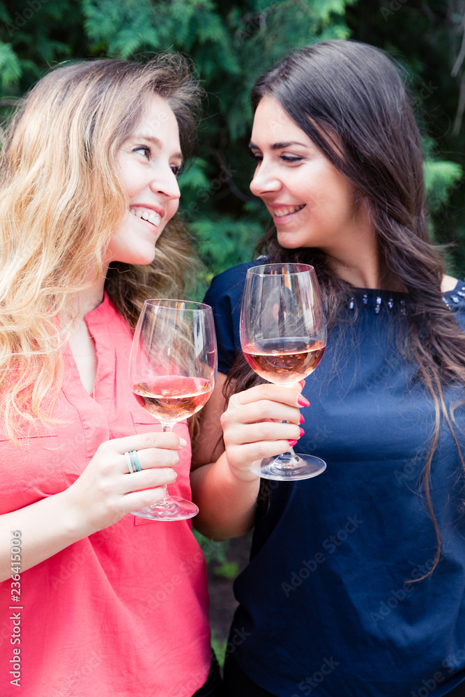 Young smiling women enjoying in a garden with glass of rose wine. Young smiling women enjoying in a garden with glass of rose wine.