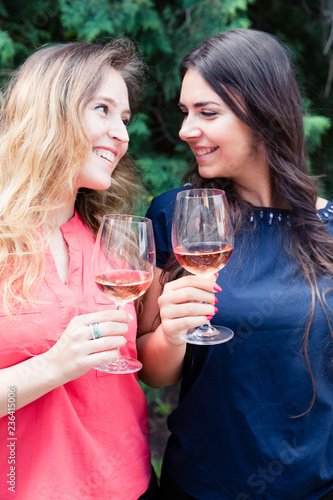 Young smiling women enjoying in a garden with glass of rose wine.