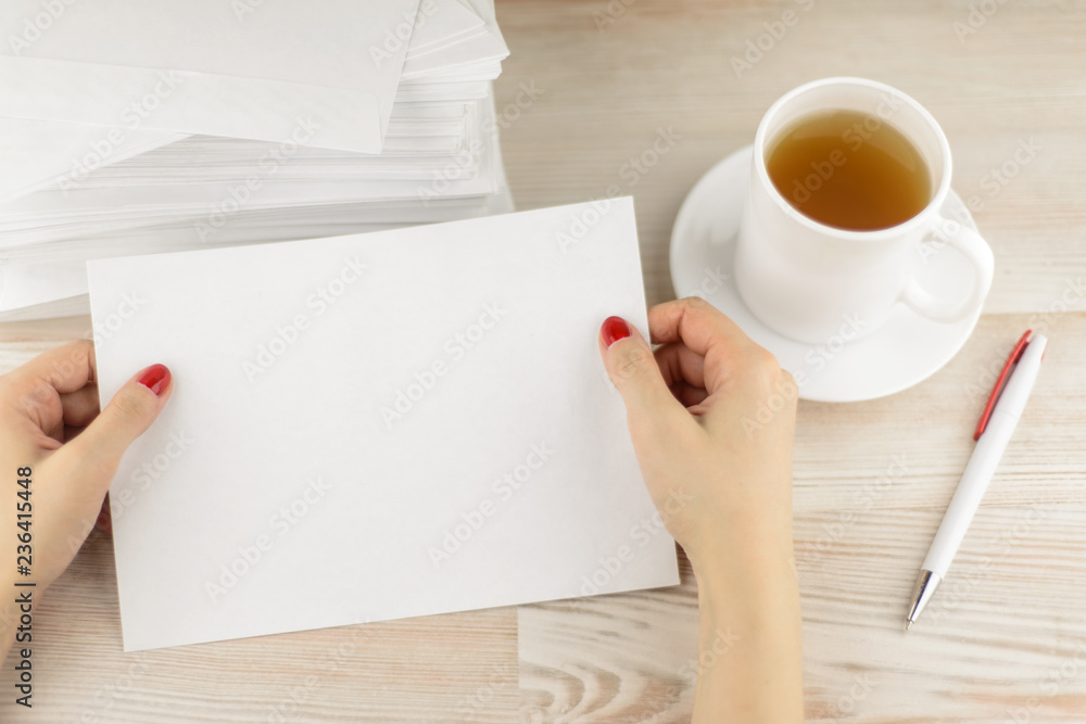 office routine: the office worker considers the form of the envelope for sending, waiting until cool fresh hot tea in a mug. A pile of empty envelopes lying behind. office routine: the office worker considers the form of the envelope for sending, waiting until cool fresh hot tea in a mug. A pile of empty envelopes lying behind.