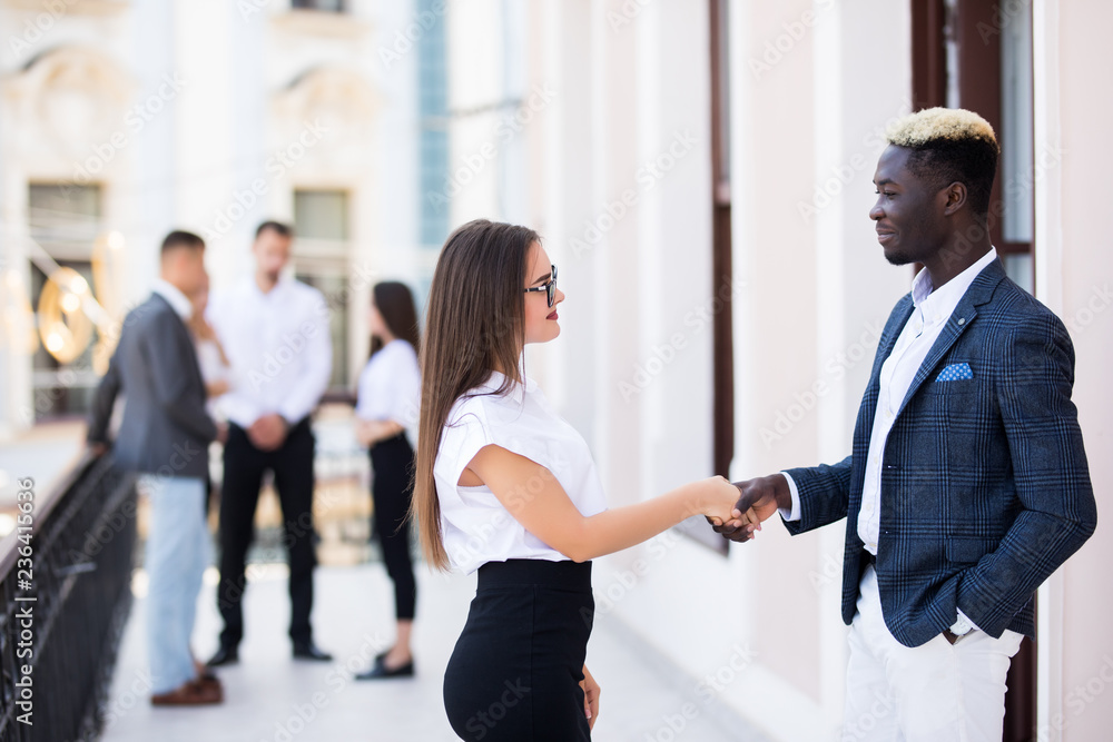 Fototapeta premium Young people of different nationalities are discussing business affairs. Handsome Afro American man and pretty caucasian woman are handshaking