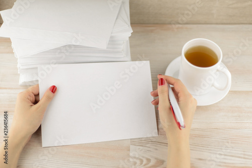 stationery everyday life: an office worker prepares to fill the blank of the envelope for sending, waiting until cool fresh hot tea in a mug. A pile of empty envelopes lying behind.