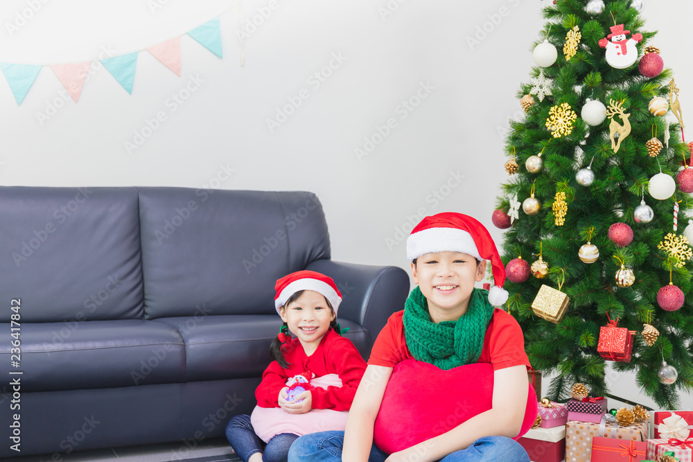 Asian boy and girl playing and decorating Christmas tree in white room at home with gift box.Smiling face and happy to celebrate festivel new year holiday with family. Asian boy and girl playing and decorating Christmas tree in white room at home with gift box.Smiling face and happy to celebrate festivel new year holiday with family.