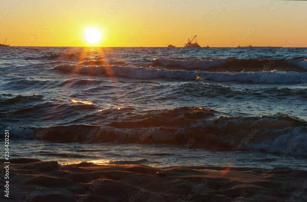 Sunset over the sea. Reflection of sunlight in the sea waves. Red and yellow sky in the rays of the sunset.