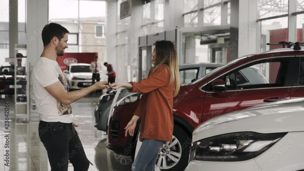 Young family at the auto salon. The husband is surprising his wife, by purchasing a nice, brand new white car. Young family at the auto salon. The husband is surprising his wife, by purchasing a nice, brand new white car.