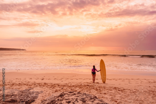 Surfer girl with surfboard at beach. Surfer woman with sunset or sunrise colors.