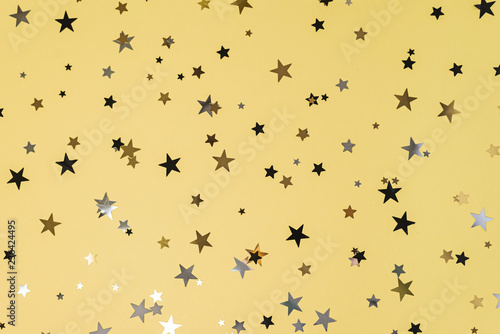 Delicate glitter star confetti on yellow background.