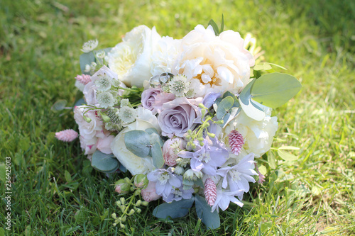 Beautiful wedding bouquet on the background of green grass in the sun. Wedding rings on a wedding bouquet