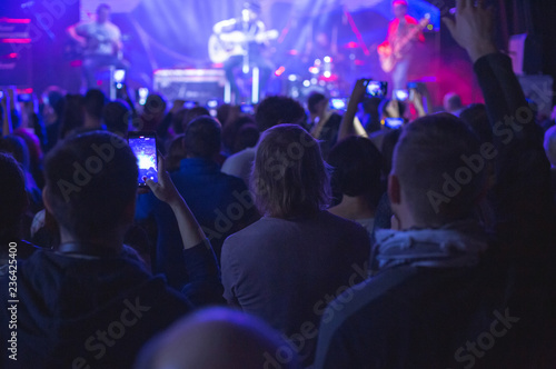 Concert crowd with arms raised, silhouettes of people with smartphones.