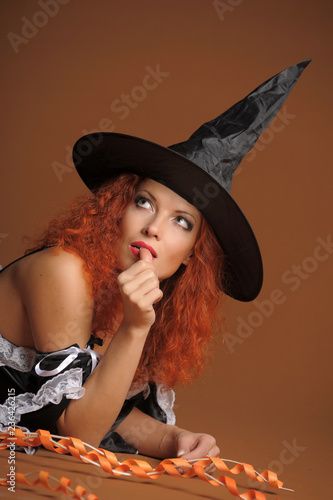 Young woman with red hair in withch costume on dark orange background photo