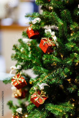 Photo of decorated Christmas spruce with red gift boxes in store.