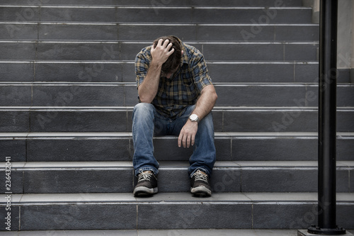 Obraz na plátně young sad and desperate man sitting outdoors at street stairs suffering anxiety