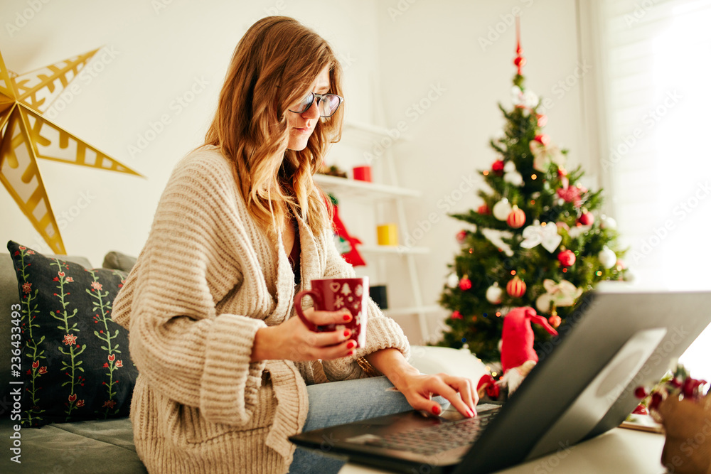 Woman holding cup of coffee while working on laptop at home for Christmas. New Year and Xmas concept. Woman holding cup of coffee while working on laptop at home for Christmas. New Year and Xmas concept.