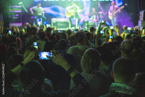 Concert crowd with arms raised, silhouettes of people with smartphones.