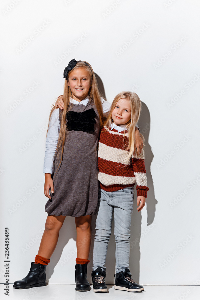 The portrait of cute little and girls in stylish jeans clothes looking at camera against white studio wall. Kids fashion and happy emotions concept The portrait of cute little and girls in stylish jeans clothes looking at camera against white studio wall. Kids fashion and happy emotions concept
