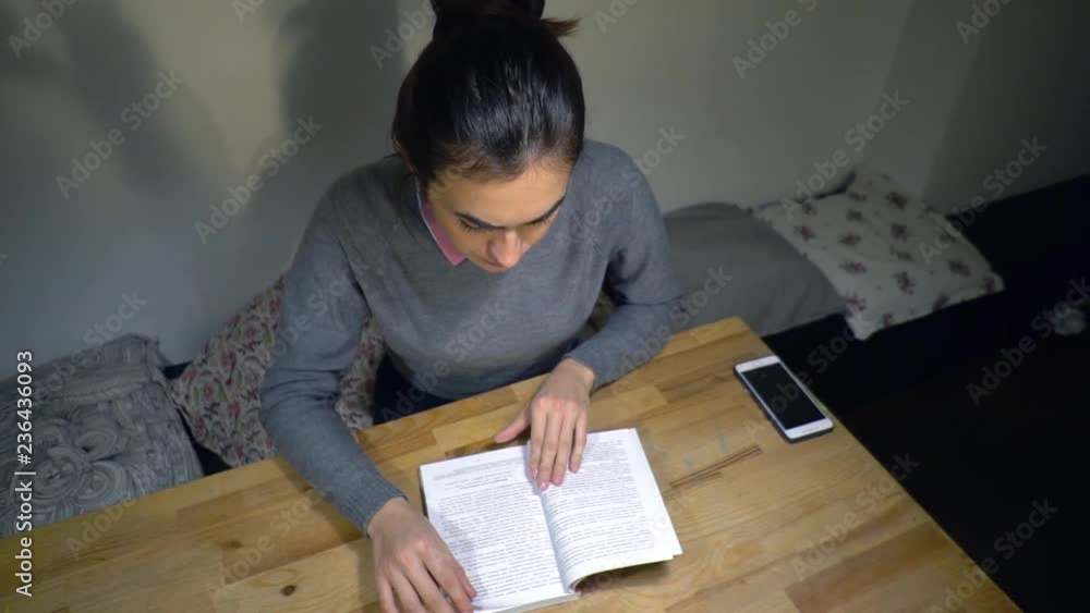 Young brunette woman reads a book while sitting at the table Young brunette woman reads a book while sitting at the table
