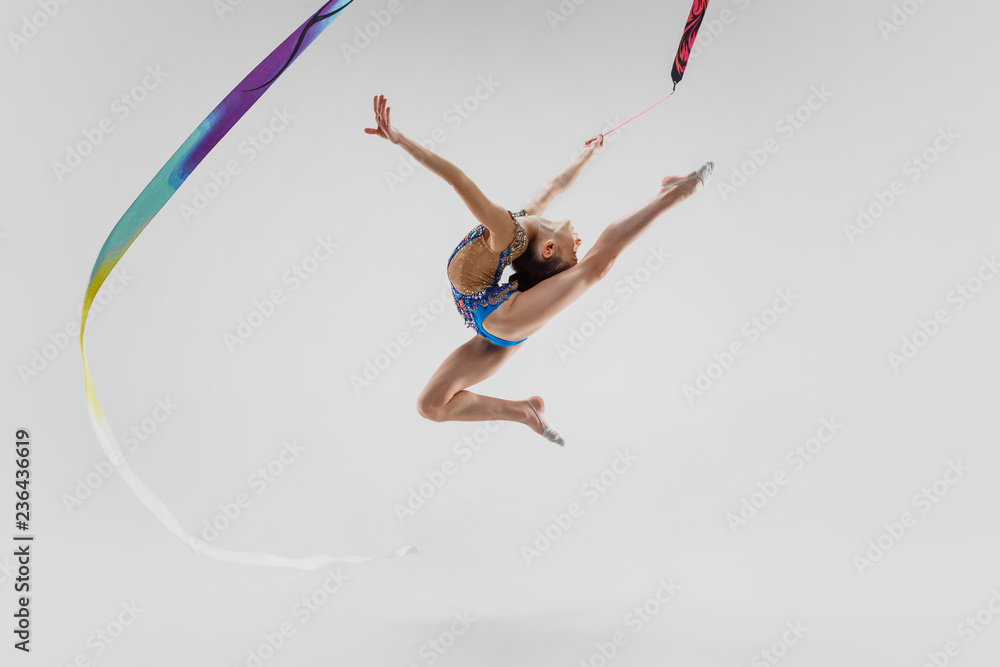 The portrait of beautiful young brunette woman gymnast training calilisthenics exercise with blue ribbon on white studio background. Art gymnastics concept. Caucasian model in full height