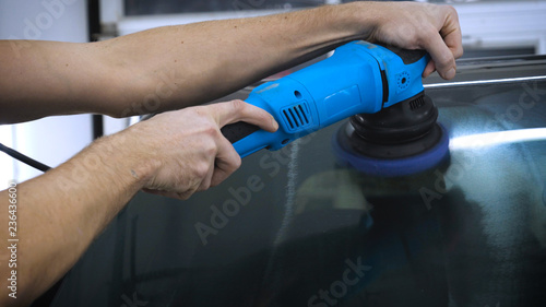 A professional worker in the automotive service handles polished glass using a polishing tool. Concept from: Car Garage, Auto Workshop, New Polished, Nano Protection.