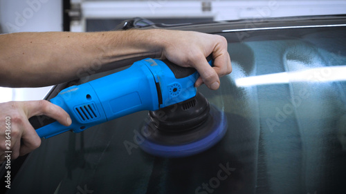 A professional worker in the automotive service handles polished glass using a polishing tool. Concept from: Car Garage, Auto Workshop, New Polished, Nano Protection.