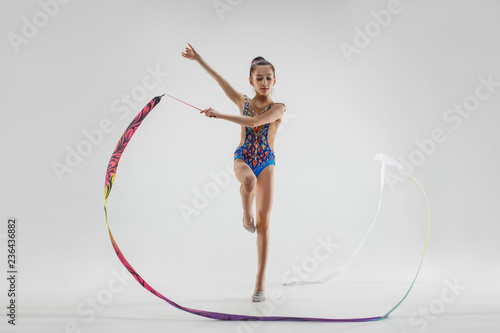 The portrait of beautiful young brunette woman gymnast training calilisthenics exercise with blue ribbon on white studio background. Art gymnastics concept. Caucasian model in full height © master1305