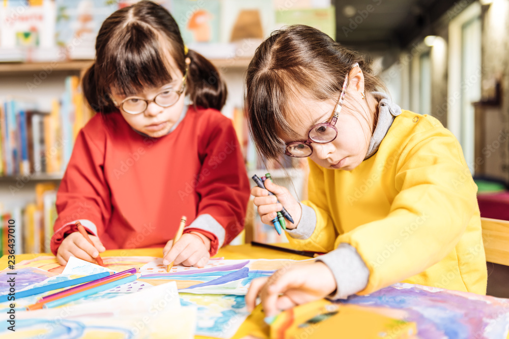 Sisters having Down syndrome feeling involved in coloring pictures Sisters having Down syndrome feeling involved in coloring pictures