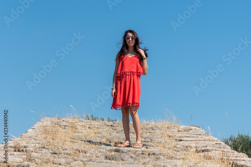 Girl in red dress and sunglasses standing on ancient bridge