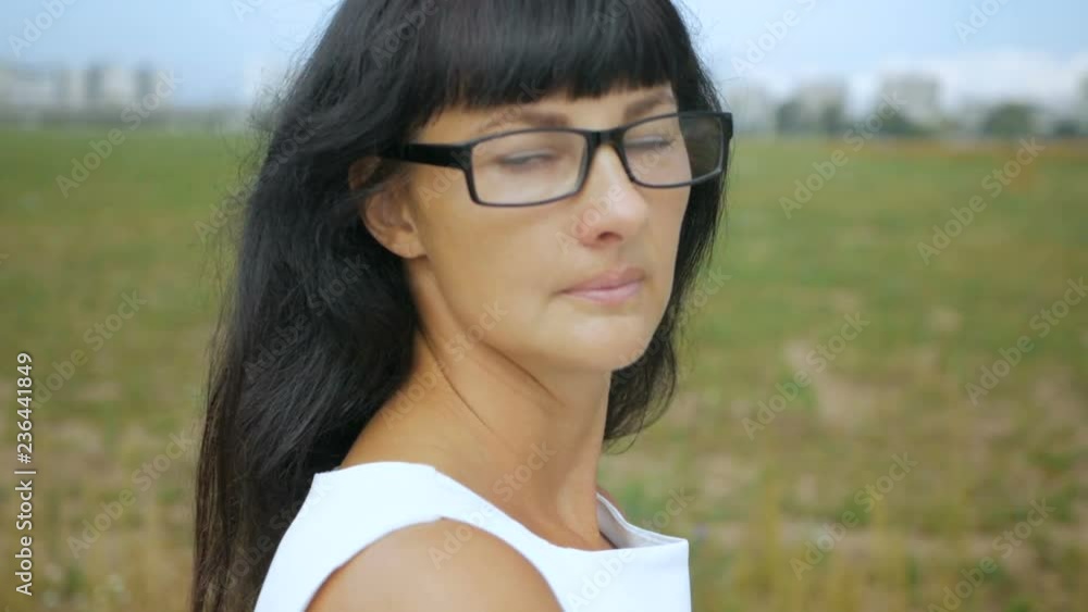 Beautiful young woman in glasses looking at camera, close-up. A woman stands on the edge of the city in a white dress. Beautiful young woman in glasses looking at camera, close-up. A woman stands on the edge of the city in a white dress.