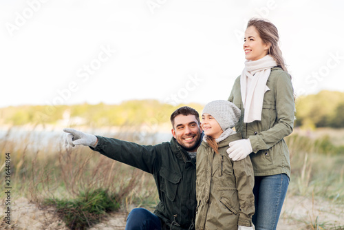 family, leisure and people concept - happy mother, father and little daughter on autumn beach
