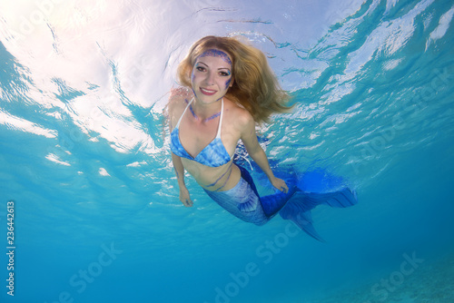 Funny golden-haired mermaid swims underwater surface in blue water, Indian Ocean, Maldives