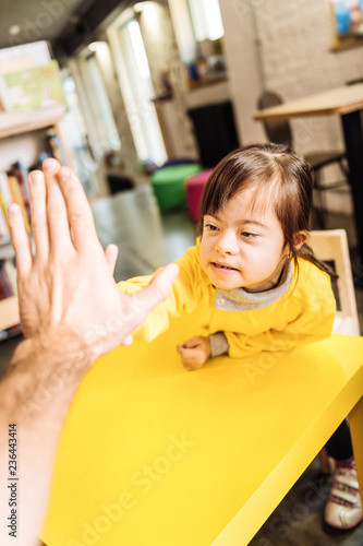 Dark-eyed girl with Down syndrome giving high five to her father