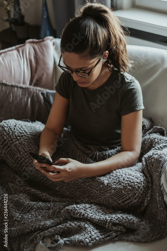 Serious girl sitting on the couch looking at mobile phone