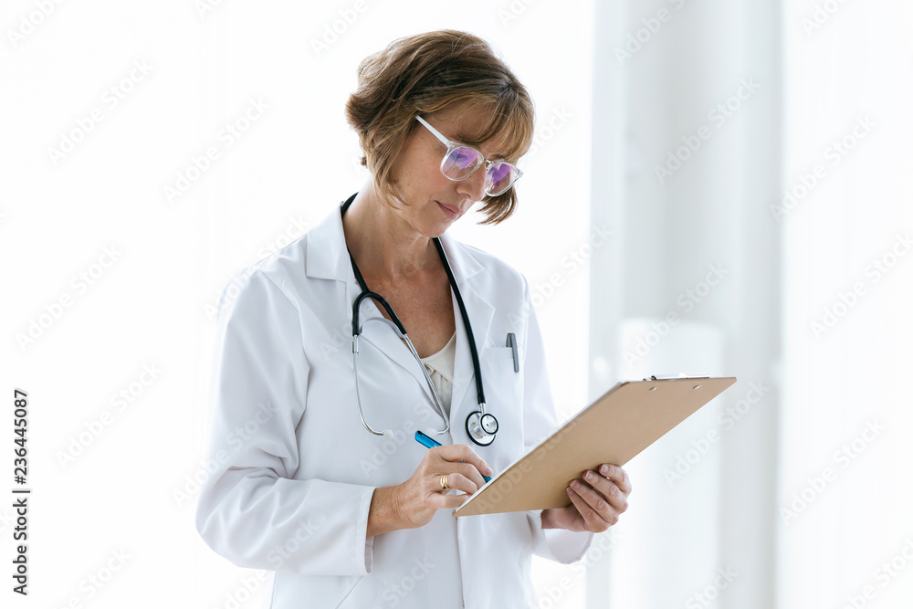 Concentrate female doctor with eyeglasses reviewing medical reports in the office at hospital. Concentrate female doctor with eyeglasses reviewing medical reports in the office at hospital.
