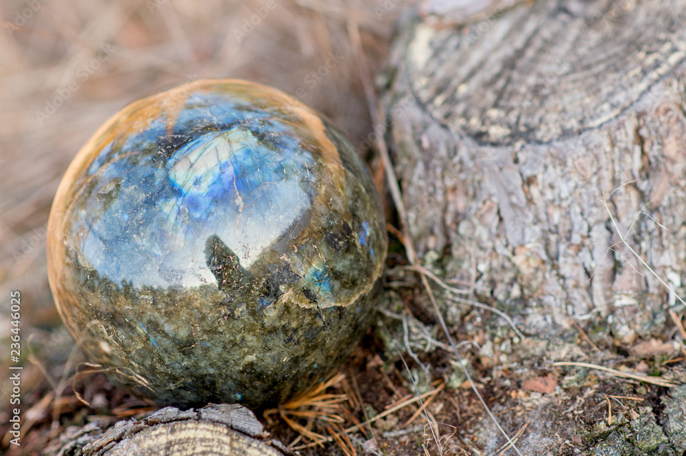 Labradorite ball stone laying in the grass and showing green and blue colors Labradorite ball stone laying in the grass and showing green and blue colors