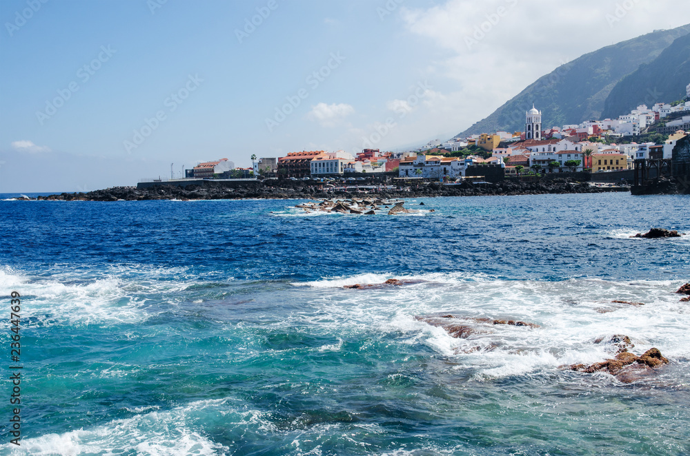 Fototapeta premium View of the town of Garachico from the ocean. Natural rock pools, old historical buildings and Santa Ana church on the background. Tenerife North, Canary Islands, Spain. 