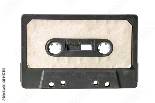 An old vintage cassette tape from the 1980s (obsolete music technology). Black plastic body, old worn textured paper label, isolated on white.
