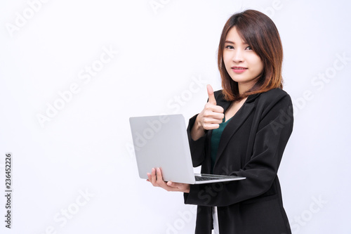 Attractive business young woman holding laptop standing on isolated white background. Portrait of beautiful young girl showing thumb up for success looking at camera against white background.