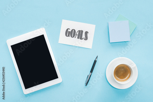 top view of digital tablet with blank screen, 'goals' lettering on card and sticky notes with blue background