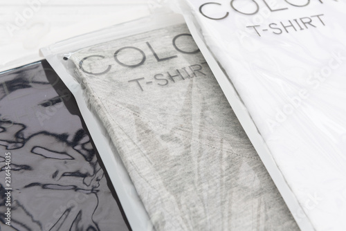 New black, white and grey v neck shirt in plastic wrap  on white wooden background