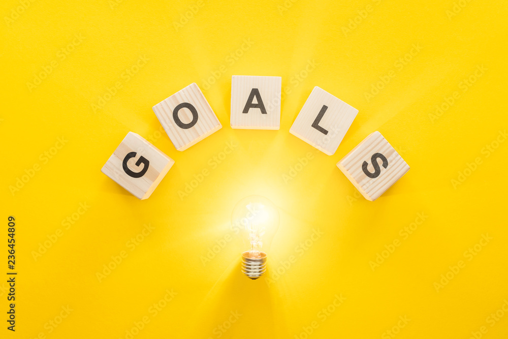 top view of glowing light bulb under 'goals' word made of wooden blocks on yellow background, goal setting concept top view of glowing light bulb under 'goals' word made of wooden blocks on yellow background, goal setting concept