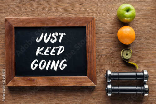 Fototapeta Naklejka Na Ścianę i Meble -  fruits, dumbbells, measuring tape and wooden chalk board with 'just keep going' quote, dieting and healthy lifesyle concept