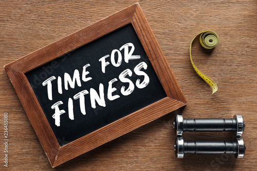 measuring tape, dumbbells and wooden chalk board with 'time for fitness' quote, dieting and healthy lifesyle concept