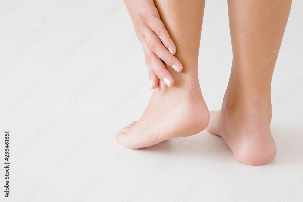 Young woman's hand touching perfect groomed legs on gray background. Tired feet. Care about clean, soft, smooth skin. Close up. Back view. Young woman's hand touching perfect groomed legs on gray background. Tired feet. Care about clean, soft, smooth skin. Close up. Back view.