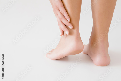 Young woman's hand touching perfect groomed legs on gray background. Tired feet. Care about clean, soft, smooth skin. Close up. Back view. © fotoduets